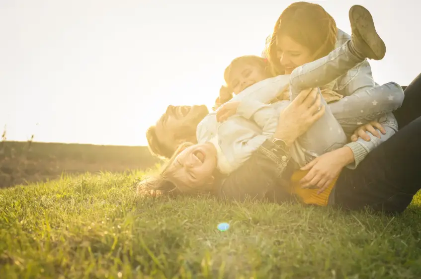 Happy family feeling safe and protected rolling around in grass Synergy Insurance KS